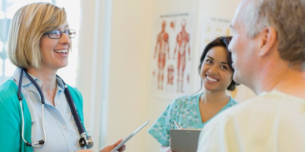 Happy female doctor and nurse discussing with male patient in clinic